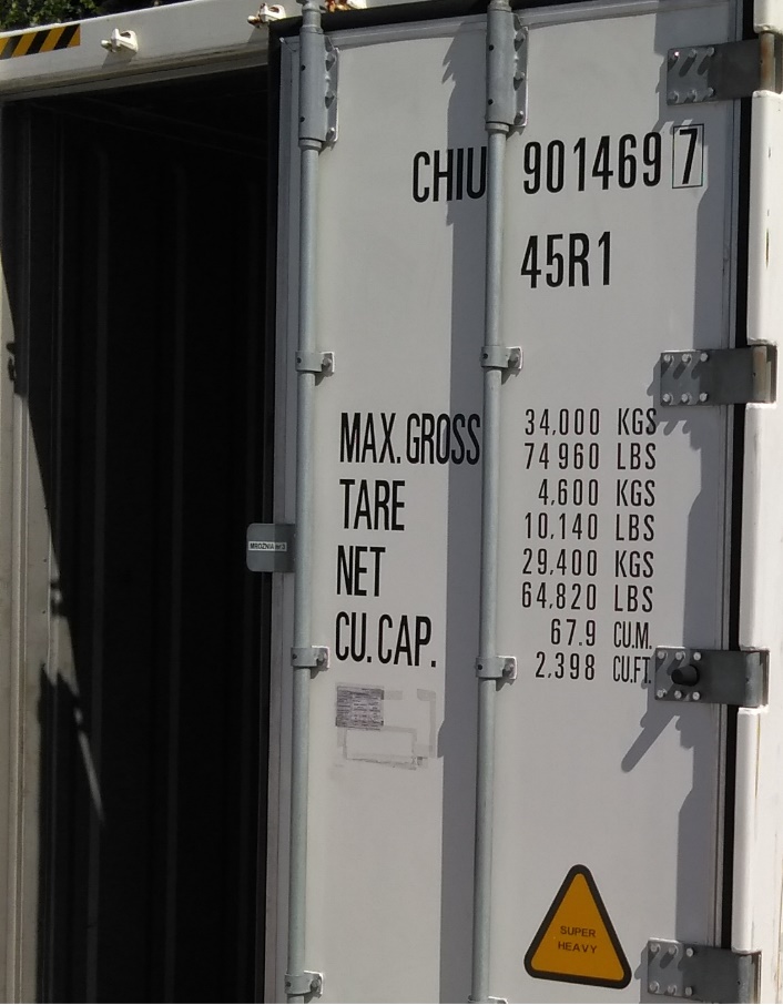 Zdjęcie przedstawia uchylone drzwi od kontenera z różnymi technicznymi napisami i liczbami